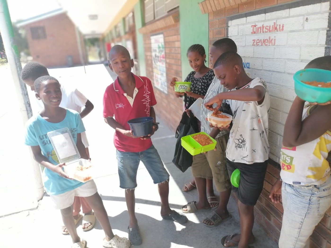 Children outside a school holding containers of food